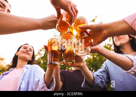 Groupe d'amis heureux clinquant des verres de bière à l'extérieur, vue de dessous Banque D'Images