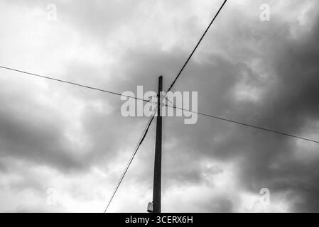 Image en noir et blanc d'un poteau de service avec des câbles électriques qui se croisent sous des nuages spectaculaires. Une photo minimaliste et à fort contraste évoquant la tension, Struc Banque D'Images