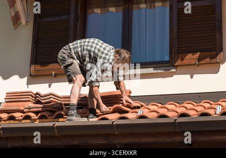 Couvreur inspectant et réparant le toit par une journée ensoleillée. Concept d'entretien de la maison, de réparation de toiture, de travaux de construction et de sécurité des bâtiments. Banque D'Images