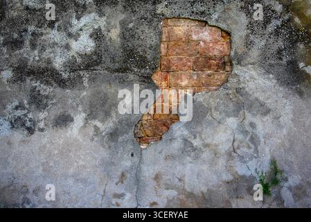 Vieux mur de plâtre altéré avec une grande fissure exposant des briques rouges en dessous. Texture urbaine, surface vieillie et pourriture naturelle parfaite pour les arrière-plans, desig Banque D'Images