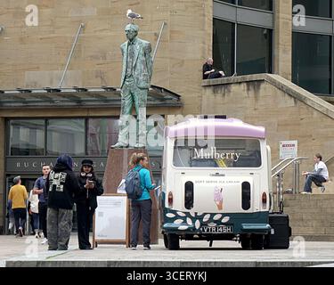 Glasgow, Écosse, Royaume-Uni. 19 août 2025. Météo au Royaume-Uni : les températures ont chuté et il s'est assombri pour la journée mondiale de la photographie dans le centre de la ville. La chaîne de mode Mulberry distribuait gratuitement de la glace de créateur à l'ombre de la statue de robert Dewar près des marches du hall du cncert avec une mouette regardant avariablement. Crédit Gerard Ferry/Alamy Live News Banque D'Images