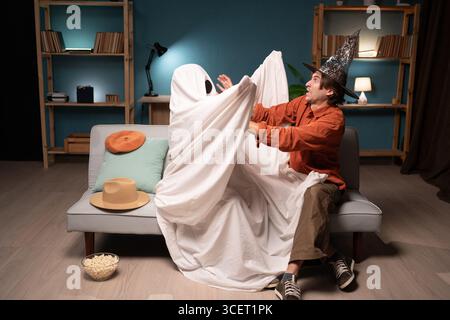 Homme et personne méconnaissable en costume de fantôme avec des yeux noirs s'amusant à la maison pendant la veille d'Halloween. Moment effrayant mais joyeux. Fête effrayante Banque D'Images