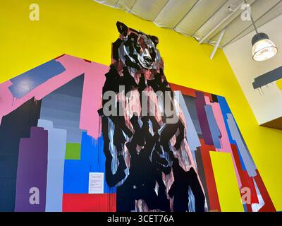 Murale abstraite d'ours peinte sur un mur jaune vif, avec des formes géométriques audacieuses en rose, bleu, rouge, gris et noir. Banque D'Images