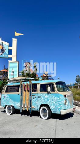 Un camping-car Volkswagen rétro décoré avec un design inspiré du surf, garé avec des planches de surf attachées sur le côté à une attraction en bord de mer, Californie Banque D'Images