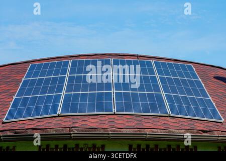 Panneaux solaires installés sur un toit rouge incurvé sous un ciel bleu clair, mettant en valeur l'énergie renouvelable, l'architecture moderne et des solutions de vie durable Banque D'Images
