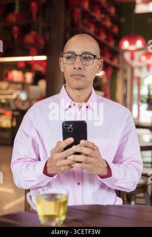 Homme mature hispanique chauve dans les années 40 portant une chemise d'affaires décontractée rose et des lunettes dans un restaurant de maison de thé de style chinois. Concept de culture, relaxati Banque D'Images