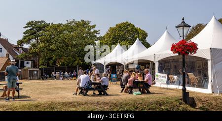 Foire d'art en plein air. Art sur le vert Milford sur la mer Hampshire avec des gens assis et profiter de l'atmosphère ensoleillée près de tentes blanches entourées d'arbres Banque D'Images