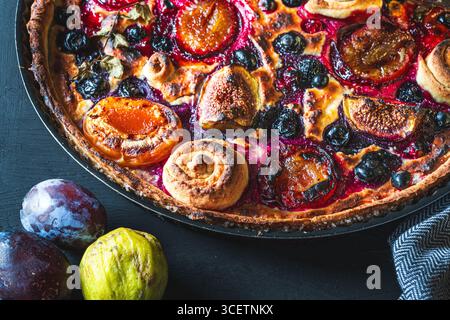 Une tarte ou une tarte ouverte avec des myrtilles, des figues, des pruneaux et des abricots dans un plat allant au four sur un fond gris. Gros plan. Photo de haute qualité Banque D'Images
