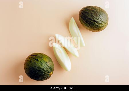 Deux melons Piel de sapo entiers avec trois tranches sur fond beige. Vue de dessus, pose à plat. Banque D'Images