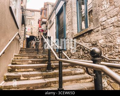 Une ruelle étroite avec un escalier menant à un bâtiment. Les escaliers sont en pierre et la balustrade en métal. Banque D'Images