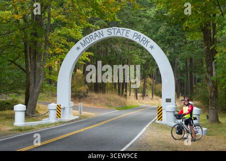 Homme de race blanche à maturité par l'entrée permanent cycliste arch pour Moran State Park, Orcas Island, San Juan County, Washington, USA Banque D'Images