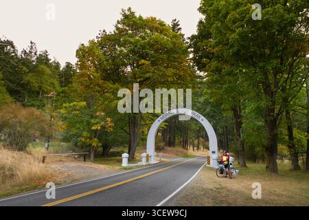 Homme de race blanche à maturité par l'entrée permanent cycliste arch pour Moran State Park, Orcas Island, San Juan County, Washington, USA Banque D'Images
