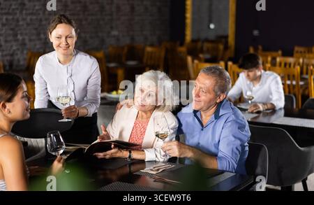 Serveuse apportant du vin à un couple de personnes âgées en choisissant des plats du menu Banque D'Images