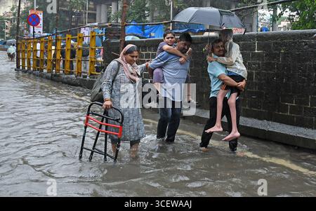 Mumbai, Maharashtra, Inde. 19 août 2025. Les hommes portent les membres de leur famille alors qu'ils traversent une rue inondée causée par les fortes pluies à Mumbai. Le trafic sur la route, la ligne de chemin de fer ont été retardés en raison de fortes pluies et des inondations sur la route et la voie ferrée sont apparues. Les écoles et les collèges sont restés fermés et de nombreux bureaux ont permis à leurs employés de travailler à domicile. Alerte rouge a été émise par le Département météorologique indien (IMD) avertissant de précipitations extrêmement fortes jusqu'à mercredi, les citoyens ont été informés de ne pas s'aventurer dehors sauf si nécessaire. (Crédit image : © Ashish Vaishnav/SOPA images via ZUMA Press Wire) EDITORIAL Banque D'Images
