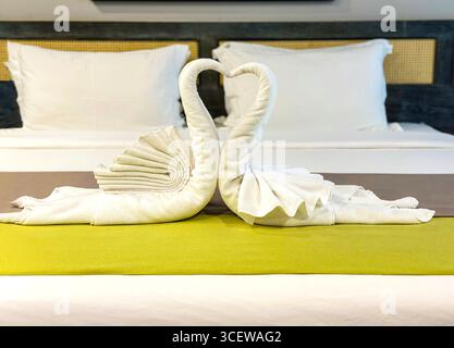 Deux cygnes de serviette blanche délicatement pliés formant une forme de coeur, élégamment posés sur un lit d'hôtel avec un coureur vert Malacca malaysia Banque D'Images