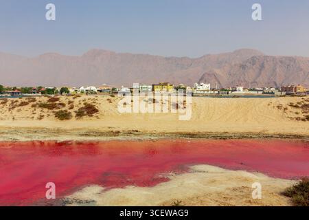 Le lac rose sur l'île de Saraya à Al Rams, Ras Al Khaimah, eau, vue sur le paysage de l'étang rouge avec des dunes de sable, les bâtiments de la ville Al Rams et les montagnes Hajar Banque D'Images