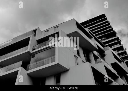 Vue en noir et blanc d'une tour résidentielle avec balcons superposés et végétation au-dessus d'un bloc secondaire à Amsterdam, pays-Bas, sous les nuages. Banque D'Images