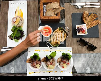 Vue du dessus de la table d'une collation saine et fraîche variée présentée dans l'assiette. Main de femme prenant l'anneau de fruits de mer frits et le trempant dans une sauce épicée Banque D'Images