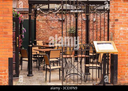 Charmant coin salon de café extérieur avec tables et chaises entourées de murs de briques et une porte décorative en fer forgé, parfait pour l'hospitalité et di Banque D'Images