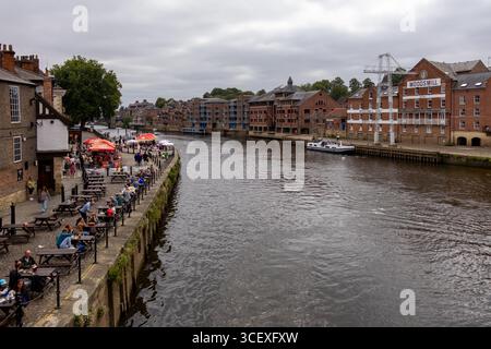 Scène fluviale animée à York, en Angleterre, avec des gens qui dînent dans des cafés et restaurants en plein air le long du front de mer. Vue des bateaux, bâtiments historiques, an Banque D'Images