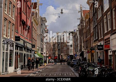 Grandes maisons en briques avec des magasins et des vélos stationnés, les gens marchant et faisant du vélo sous des lampes suspendues et des nuages sur Haarlemmerdijk, rue à Amsterdam. Banque D'Images