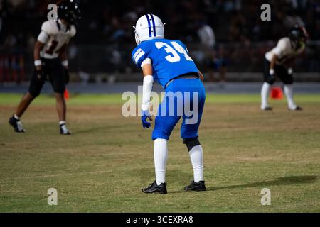 Football américain défensive back joueur de football en uniforme bleu numéro 34 accroupis dans une position prête sous les lumières du stade, concentré et préparé Banque D'Images
