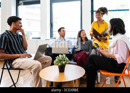 Équipe diversifiée de professionnels collaborant dans un bureau moderne, discutant de projets et partageant des idées tout en utilisant des ordinateurs portables et des documents pour favoriser Banque D'Images