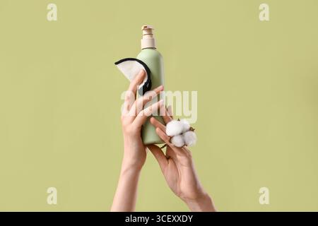 Mains féminines tenant le tampon réutilisable, bouteille de produit cosmétique et fleur de coton sur fond vert Banque D'Images