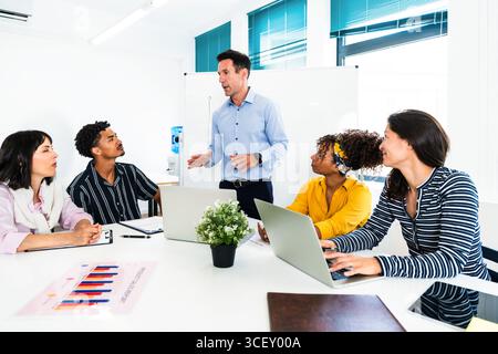Équipe diversifiée de professionnels collaborant sur un projet, s’engageant dans une discussion productive menée par leur gestionnaire dans un cadre de bureau lumineux et moderne, Banque D'Images