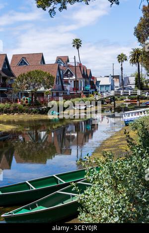 Vue de maisons pittoresques avec des toits à pignons reflétant dans les eaux tranquilles du canal, tandis que des bateaux verts reposent le long des rives sous le soleil vibrant, Los Angeles, Banque D'Images