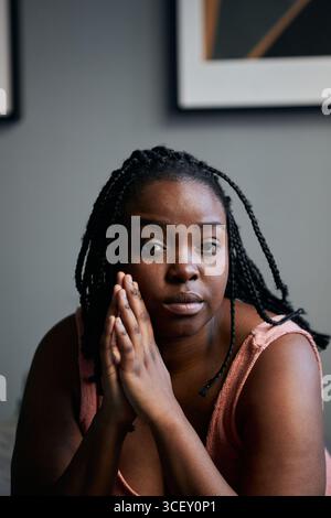 Gros plan vertical moyen de la belle jeune femme noire assise dans la chambre à coucher à la maison regardant la caméra Banque D'Images