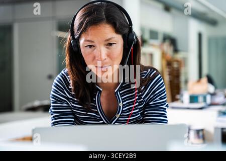 Une femme d'affaires concentrée qui porte un micro-casque travaille à distance à l'aide d'un ordinateur portable au bureau à domicile, participe à une réunion en ligne ou fournit un service client Banque D'Images