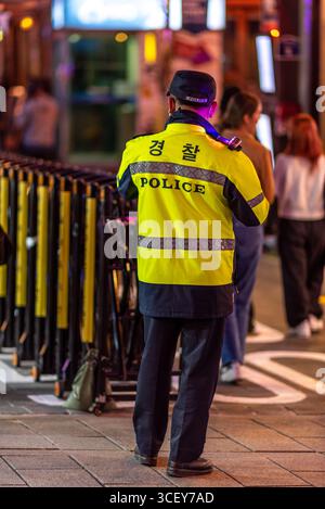 Un policier vêtu d'une veste jaune se tient debout dans une rue animée la nuit à Séoul, en Corée du Sud, le 27 octobre 2023 Banque D'Images