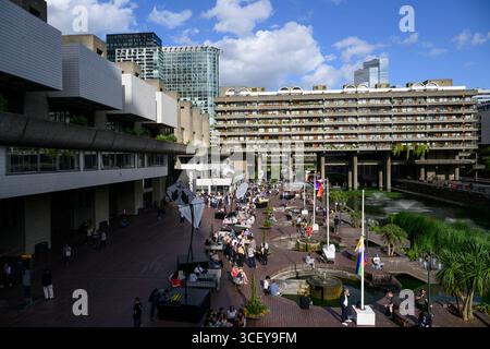 Les gens assis sur la terrasse au bord du lac en face du Barbican Centre. Le Barbican Centre est un centre des arts renommé et fait partie du domaine Barbican. Banque D'Images