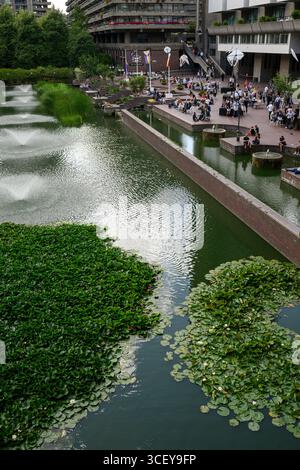 Les gens assis sur la terrasse au bord du lac en face du Barbican Centre. Le Barbican Centre est un centre des arts renommé et fait partie du domaine Barbican. Banque D'Images