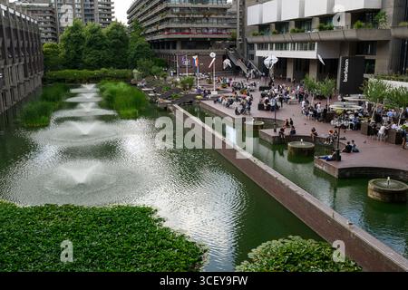 Les gens assis sur la terrasse au bord du lac en face du Barbican Centre. Le Barbican Centre est un centre des arts renommé et fait partie du domaine Barbican. Banque D'Images