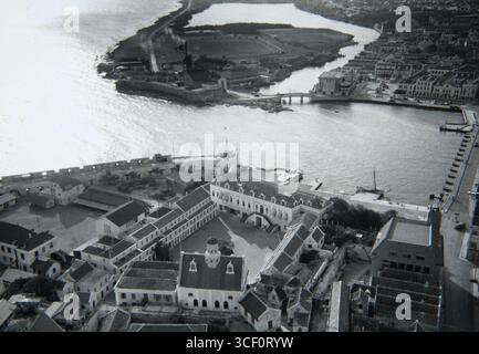 Cette photographie aérienne, prise vers 1945, montre Willemstad, Curaçao. Les principaux endroits visibles comprennent le Palais du Gouverneur, Fortkerk au Fort Amsterdam à Punda, la caserne Willem III, Waterfort, le bureau de la KNSM et le pont Queen Emma reliant Punda à Otrabanda. L'image capture la disposition de la ville, y compris Brionplein et la zone de Rifwater avant qu'elle ne soit remplie. Banque D'Images
