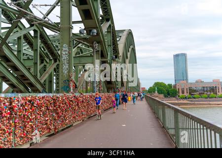 Cologne, Allemagne - 15 juin 2025 : écluses vives décorant les balustrades du pont Hohenzollern, avec l'horizon de Cologne en arrière-plan et un piéton Banque D'Images