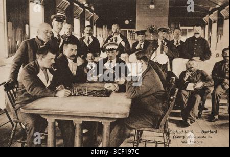 Une carte postale de propagande de la première Guerre mondiale représentant des prisonniers allemands blessés dans la salle de loisirs du camp de prisonniers de guerre de Dartford, se livrant aux échecs, lisant ou fumant une pipe. Capturé entre 1914 et 1918. Banque D'Images