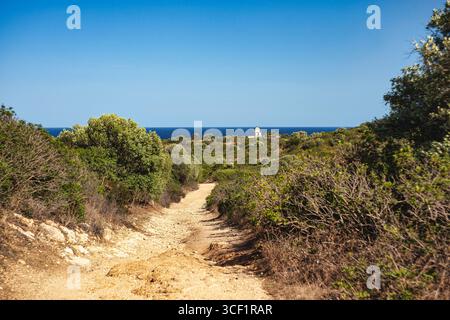 Vue panoramique sur un chemin de terre menant à un phare blanc le long de la côte de Capo ferrato en sardaigne, italie, par une journée ensoleillée Banque D'Images