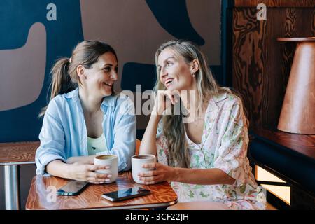 Deux jolies femmes caucasiennes assises dans un café qui parlent et rient. Banque D'Images