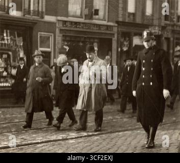 Une photographie de 1922 montre la police arrêtant un troisième suspect d'un vol à la Haye. Le suspect est escorté dans les rues de la Haye par des agents, qui se rendent au poste de police pour y être interrogé. Banque D'Images