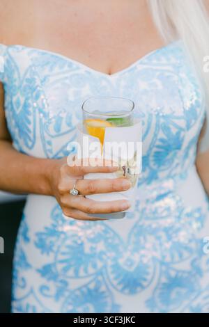 Femme dans une robe bleue profite d'une boisson fraîche avec des agrumes et de la menthe lors d'une chaude réunion d'été. Banque D'Images