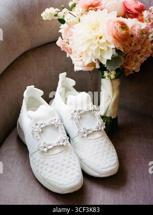 Baskets nuptiales blanches associées à un bouquet coloré sur un canapé confortable dans un espace de vie lumineux Banque D'Images