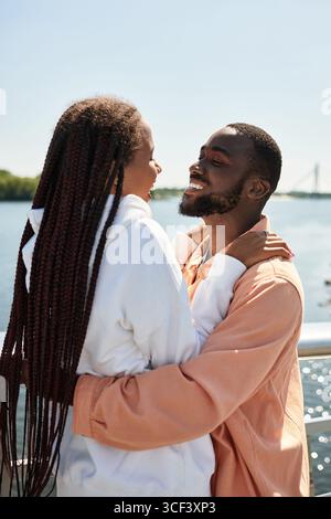 Jeune couple se promène au bord de la rivière, embrassant et riant sous le soleil chaud. Banque D'Images