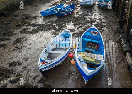 Petits bateaux bleus et blancs dans la boue amarrés dans le port de Whitby à marée basse montrant une variété d'équipements de bateau et aussi des empreintes de pas dans la boue Banque D'Images