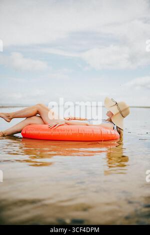 Une femme est allongée sur un radeau gonflable rouge dans l'océan. La scène est paisible et relaxante, avec la femme profitant de la chaleur du soleil et du sou Banque D'Images
