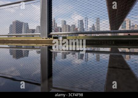 Vue sur le pont de Brooklyn et les gratte-ciel de Manhattan à travers la clôture avec des reflets urbains Banque D'Images