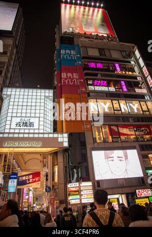 Scène nocturne animée dans le quartier Namba d'Osaka avec des néons, des panneaux d'affichage illuminés et de la foule à l'entrée de la rue commerçante Ebisu Bashi-Suji. Banque D'Images