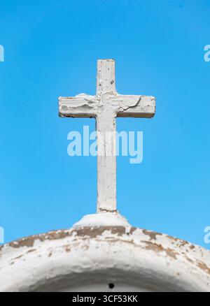 Simple croix en bois blanc avec peinture pelable debout sur un dôme blanc altéré avec un ciel bleu en arrière-plan, évoquant la spiritualité, la religion, la foi et le christianisme Banque D'Images